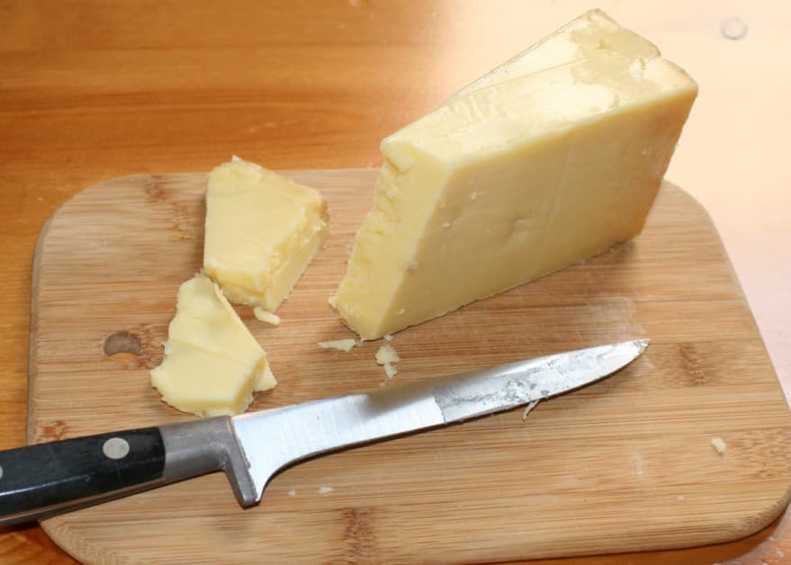 Cunha de queijo cheddar cortada sobre tábua de madeira, mostrando a cor amarela e a textura firme