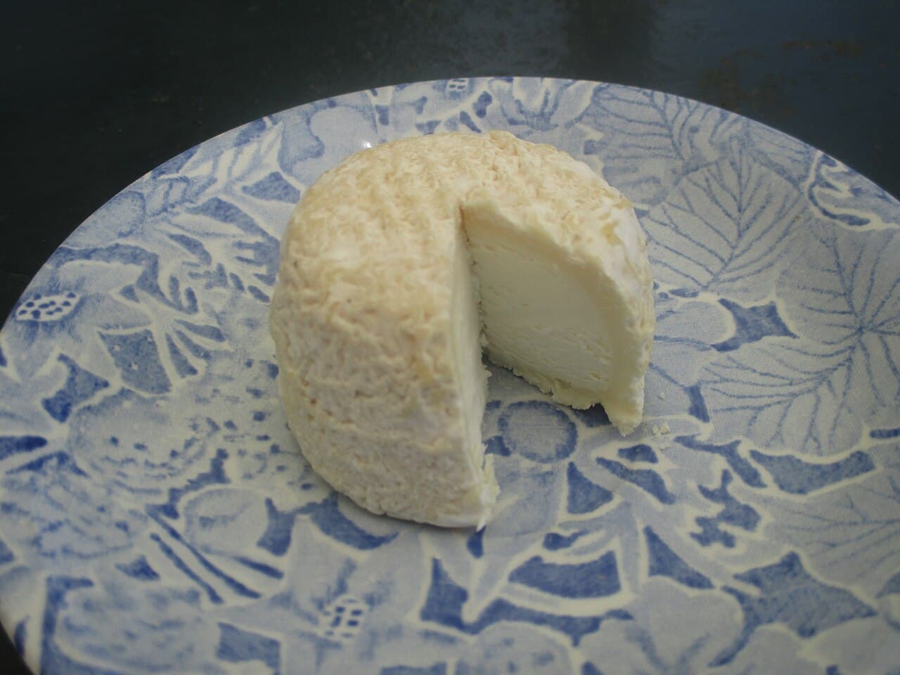 Queijo de cabra pequeno e redondo com um corte mostrando a massa branca e cremosa