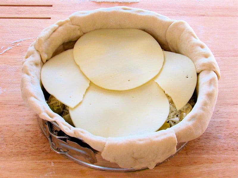 Fatias de queijo provolone sobre massa crua, prontas para ir ao forno